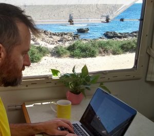 Man typing on a Macbook with view of beach through adjacent window