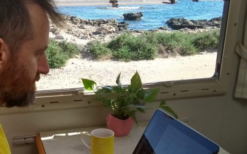 Man typing on a Macbook with view of beach through adjacent window