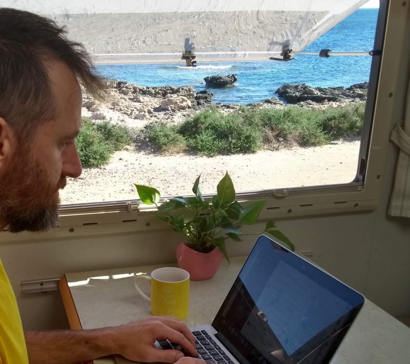 Man typing on a Macbook with view of beach through adjacent window